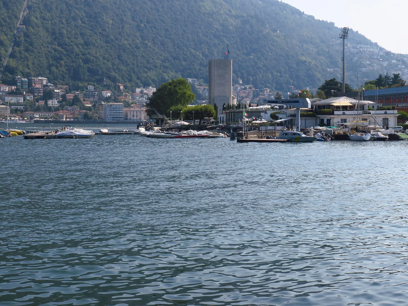 Il lungolago di Como con le barche ormeggiate e la collina di Brunate sullo sfondo