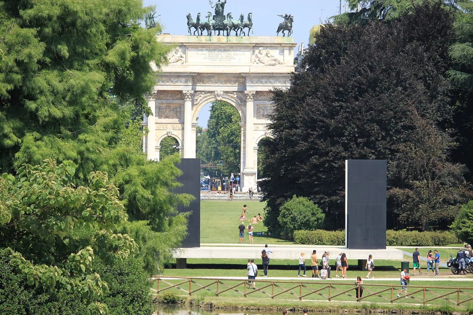 Parco Sempione in una giornata d'estate, con prati verdi, alberi e l'Arco della Pace sullo sfondo